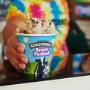 Scooper handing a fresh packed pint over the counter at a Ben & Jerry's ice cream shop.