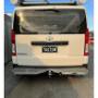 White Toyota Hiace rear with roof rack, window mesh, step platform, and towbar; plate reads TAGTOW.