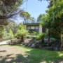 Landscaped rock gardens surround the house, providing grassy areas for children to play and established trees for shade.