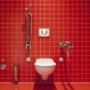 Lovely toilet fitted with red tiled background not likely to become clogged for a while due to modern fittings.