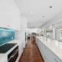 Bright white kitchen with long island, pendant lights, and blue tile splashback