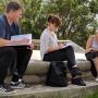 A field research session in a park setting, with participants seated on a stone bench. Two people take notes while engaging with a third person, gathering insights in a collaborative outdoor environment.