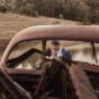Bride and Groom on there wedding day kissing framed by rustic car at ben man wedding venue by Thierry Boudan Photography