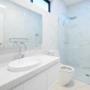 White bathroom with marble-look tiles, oval basin, and frameless glass shower