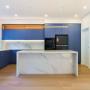 Kitchen with blue cabinetry, island bench, and backlit overheads with marble-look finishes