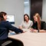 Three team members having a collaborative meeting at a desk in Trekk Rockhampton office. They're smiling and reviewing documents together, with computer monitors in the background.