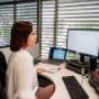 A professional woman works at her desk in Trekk Rockhampton office, focused on her computer monitor with scheduling software open. Her workspace is organised with a notebook, dual screens, and natural light from surrounding windows.