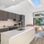 Sleek kitchen with dark cabinetry and white island under a skylight, opening to a sunny backyard dining area.