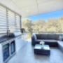 Open-plan living room and kitchen seen through bifold doors, white sofa with pink cushions, garden foreground.