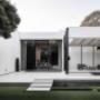 Minimalist white modern home exterior with large glass doors, black accents, and floating steps over water.